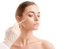 A person with long hair tied back is receiving an injection on the cheek. A gloved hand is holding the syringe. The background is white, and the person appears calm and composed.